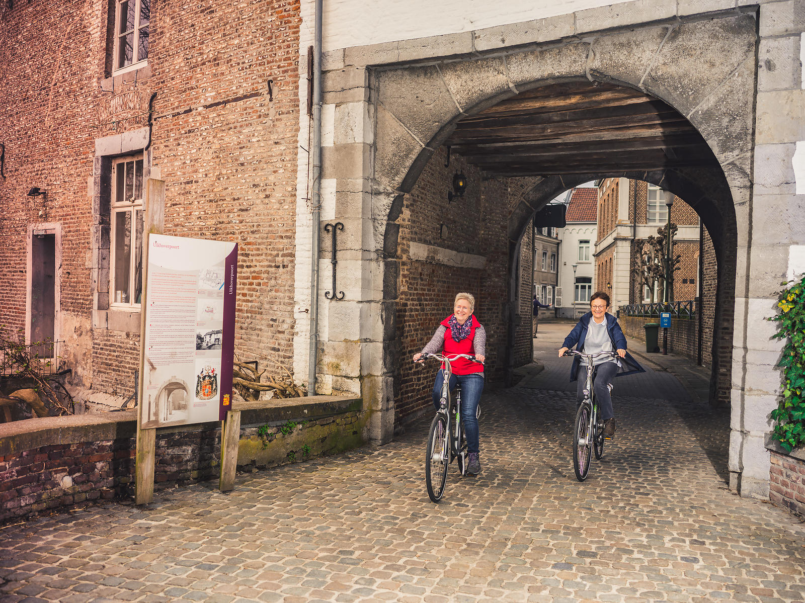 Fietsende vrouwen onder poort in Oud-Rekem ©KVDS